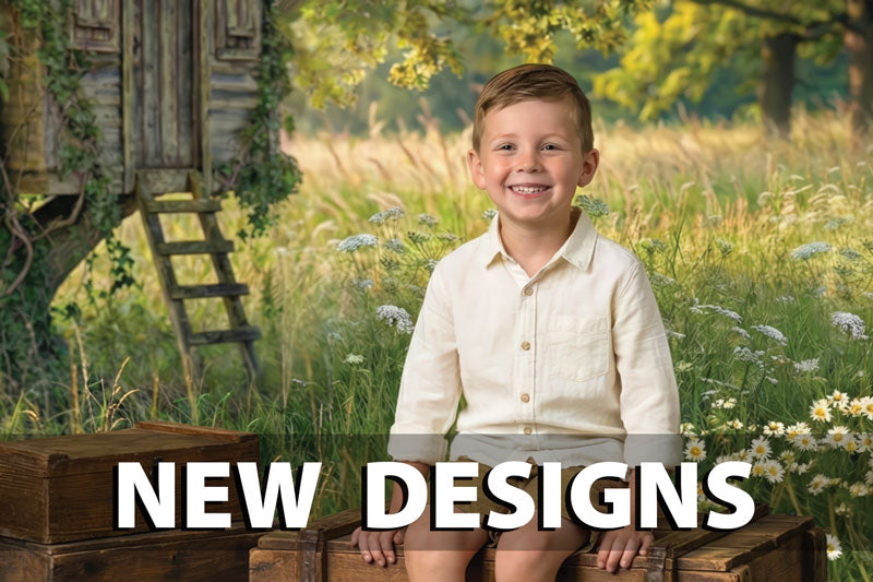 Smiling young boy wearing a light beige button-down shirt and shorts sitting on rustic wooden crates in a sunlit meadow filled with wildflowers, with a wooden treehouse and ladder in the background among tall grass and leafy trees.