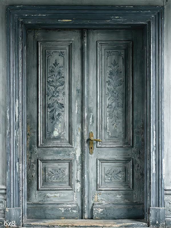 This photography backdrop shows aged gray double doors with distressed paint and subtle floral panel details set within a paneled wall, forming a refined studio background for portraits.