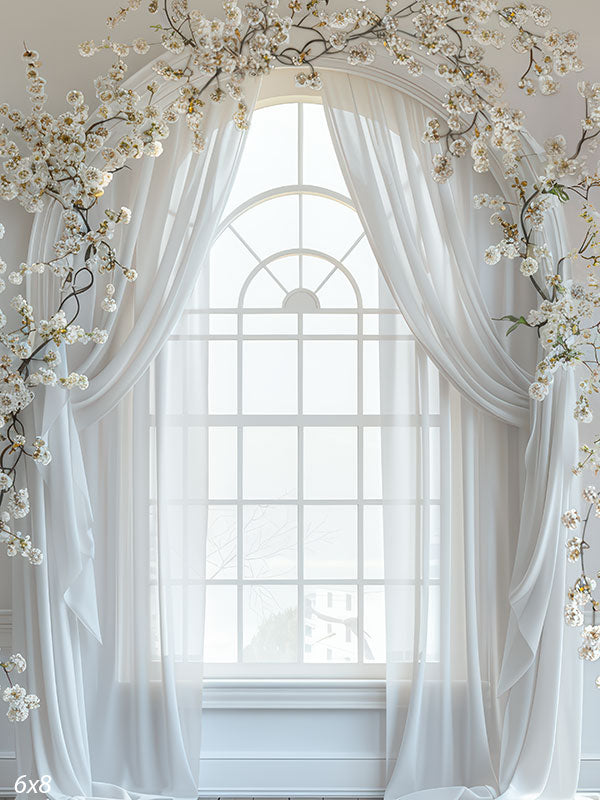Elegant white studio backdrop featuring sheer curtains over a tall arched window, framed by delicate spring floral branches for light and airy portrait sessions.