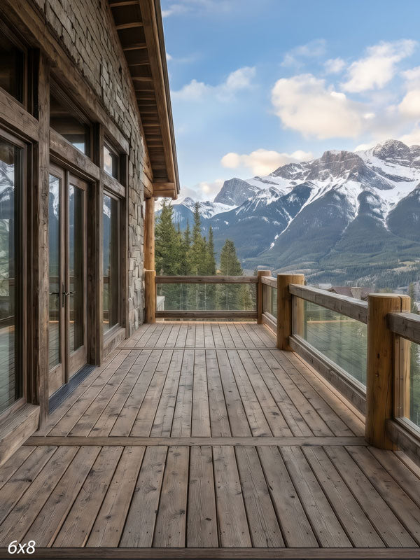 Rustic stone-and-log cabin deck with a plank floor overlooking pine forest and snow-capped mountains, a scenic photography backdrop.