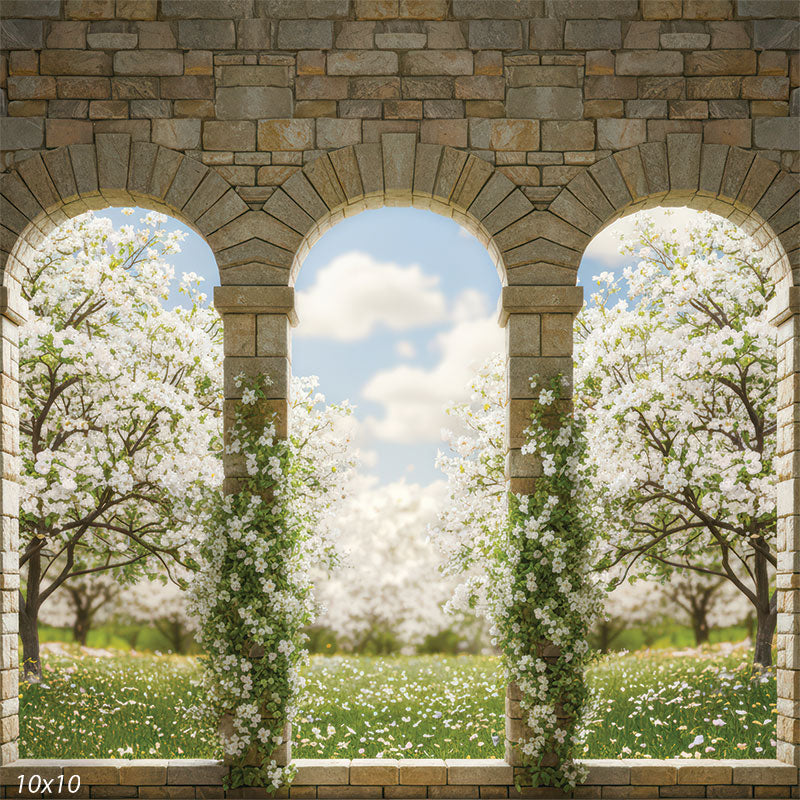 Three warm stone arches wrapped in white blossoms, overlooking a sunlit green meadow and rows of flowering spring trees under a pastel blue, cloud-filled sky.