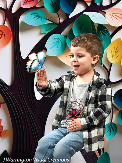 Little boy smiling as a blue butterfly rests on his finger, rainbow tree and bright leaves in background.