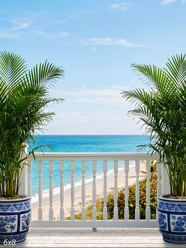 White-plank seaside deck with a spindle railing and blue-and-white porcelain planters of palms over turquoise ocean, a scenic photography backdrop.