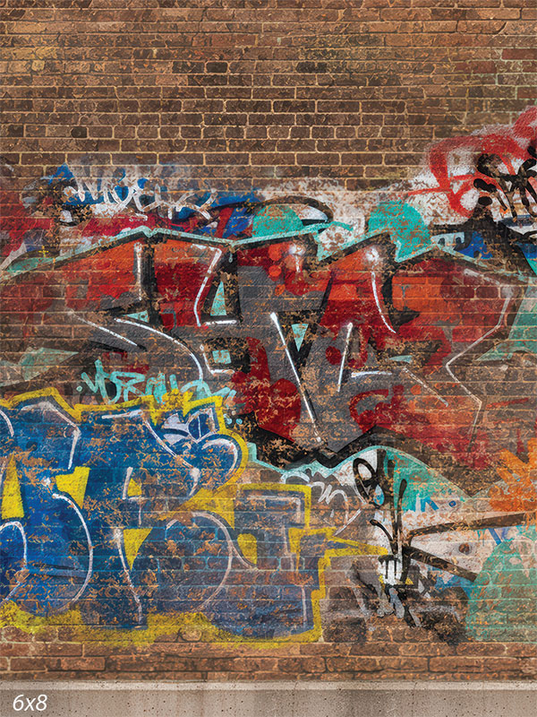 Printed photography backdrop showing a red-brown brick wall with a band of layered street graffiti across the lower portion in blues, reds, and teal. The upper area is mostly plain brick behind a subject.
