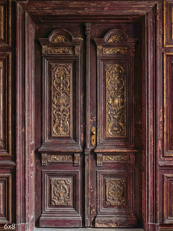 This photography backdrop shows carved burgundy double doors surrounded by paneled walls with aged paint, ornate detailing, and muted gold accents forming a studio background for portraits.