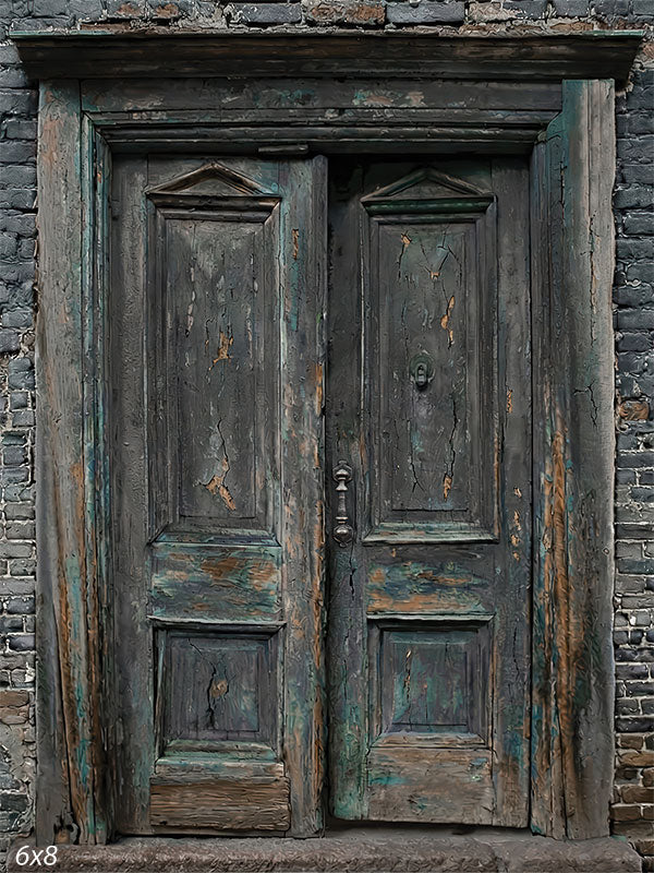 This photography backdrop shows weathered double wooden doors with peeling paint set into a dark charcoal brick wall, creating a textured studio background for portraits.