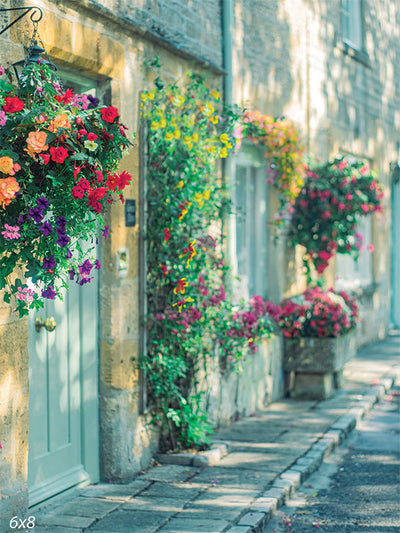 A quaint alleyway with vibrant hanging flower baskets, blooming greenery, and rustic stone walls, ideal for professional spring photography.