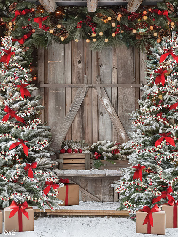 Christmas Winter Barn Photography Backdrop - Rustic barn decorated for Christmas with snow-covered trees, red bows, festive ornaments, and a garland of greenery and pinecones.