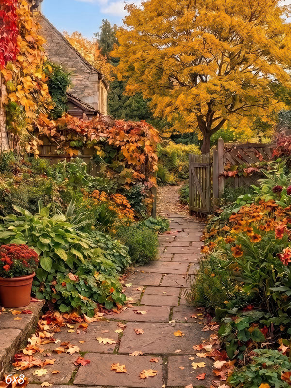 Autumn cottage garden photography backdrop with a flagstone path curving past a red ivy stone wall, potted mums, a wooden gate, and a golden maple tree.