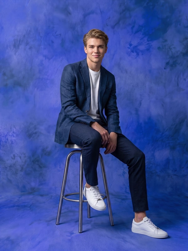 Cobalt Drift cobalt blue texture photography backdrop shown behind a young man in a navy blazer seated on a stool CP-8977