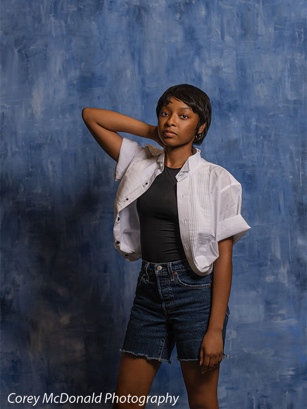 Vivid royal blue abstract hand-painted photography backdrop shown in a studio senior portrait with a young woman standing, one hand raised behind her head OM-2639