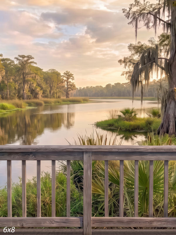 Southern bayou photography backdrop with a wooden railing overlooking a calm bayou, Spanish-moss cypress, palmetto, and a soft peach sunset sky.