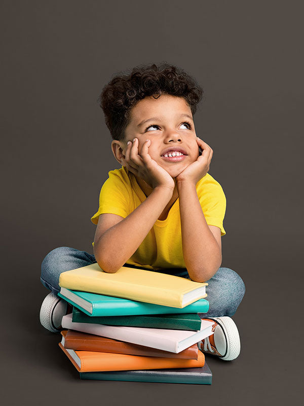 A child posing with books against a dark gray seamless photography backdrop for commercial use.