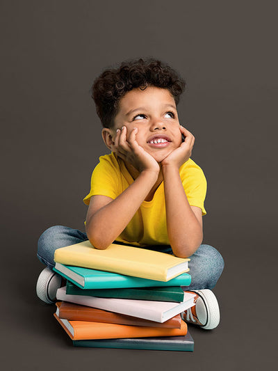 A child posing with books against a dark gray seamless photography backdrop for commercial use.