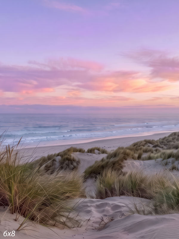 Pastel beach photography backdrop with grassy sand dunes and gentle surf under a soft pink and lavender sunset sky.