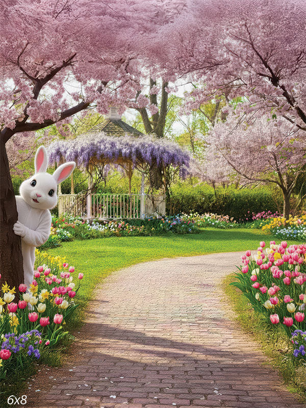 A studio background showing a brick path in a spring garden with a white bunny peeking from behind a tree. Colorful tulips and pink cherry blossoms frame the scene