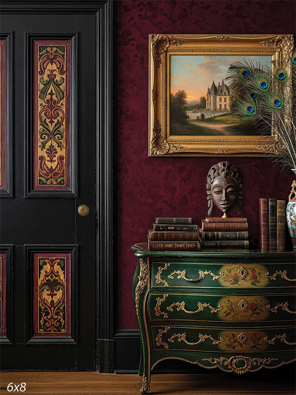 An opulent portrait backdrop featuring a black-paneled door with gold damask insets, burgundy damask wallpaper, and an ornate forest green chest with gilded accents.