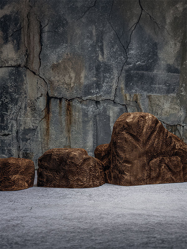 Faux rock set photo prop of textured brown boulders arranged in a row against a cracked stone quarry wall.