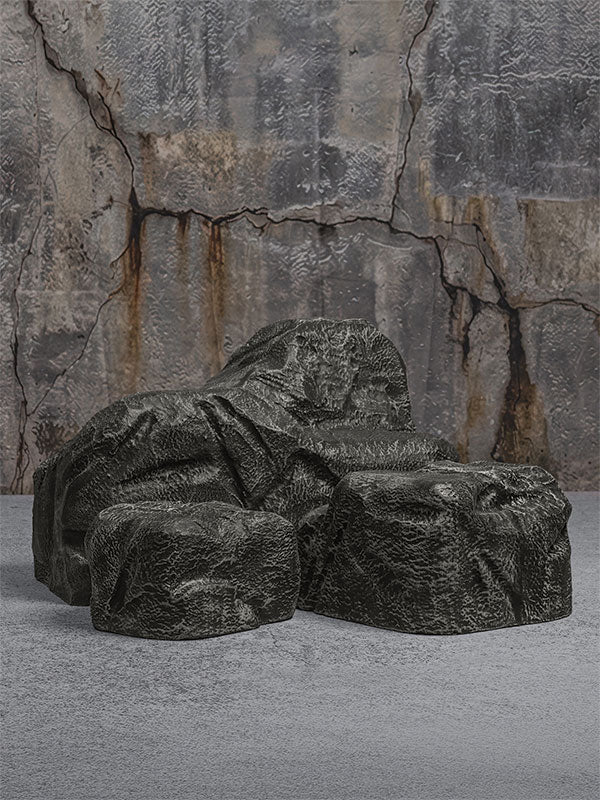 Faux rock set photo prop of textured grey boulders arranged in a low grouping against a cracked stone quarry wall.