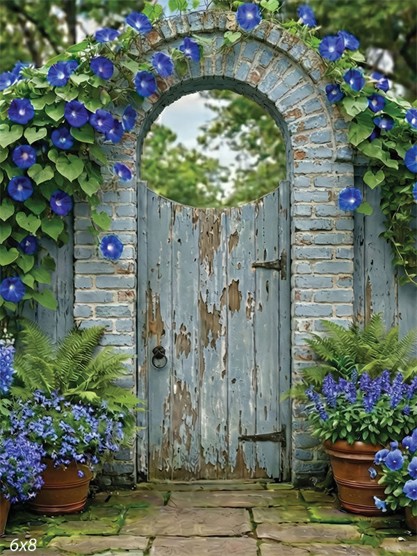 Garden photography backdrop featuring a weathered blue wooden gate framed by an arched brick entry with blue flowers and greenery.