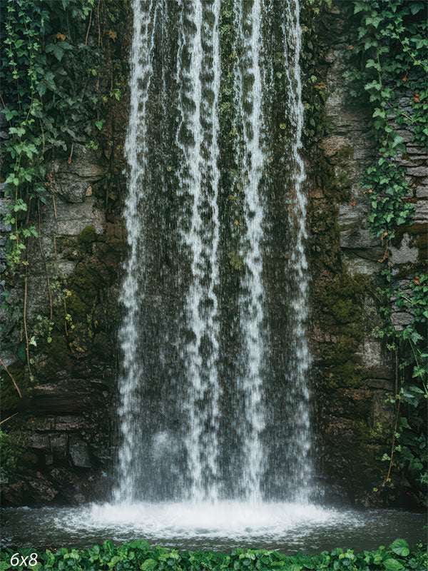 Printed photography backdrop showing a vertical waterfall flowing down a stone wall with moss and ivy along both sides. A small dark pool sits at the base beneath the falling water.