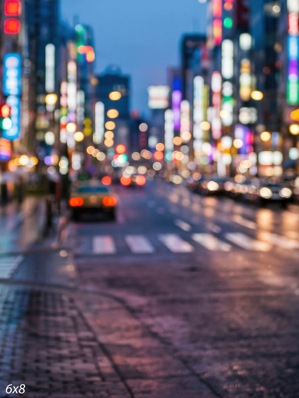 City street at dusk rendered out of focus into multicolored bokeh light orbs over a softly reflective road, a bokeh photography backdrop.