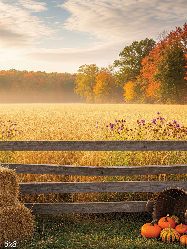 A scenic photography backdrop of a golden wheat field with a rustic fence, pumpkins, and vibrant fall foliage under a glowing sky.