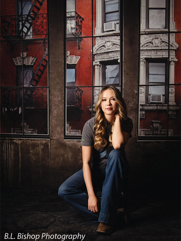 Editorial-style senior photo backdrop with moody urban brick and industrial window design.