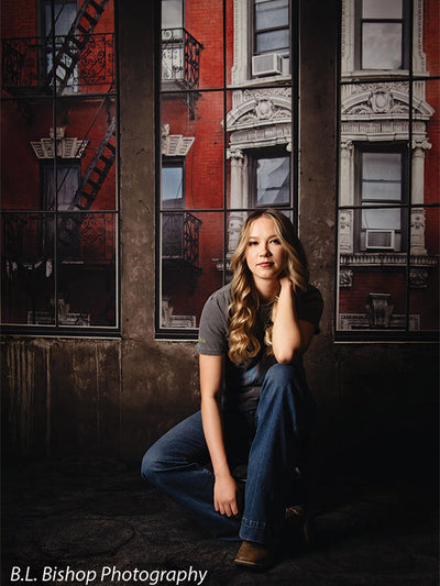 Editorial-style senior photo backdrop with moody urban brick and industrial window design.
