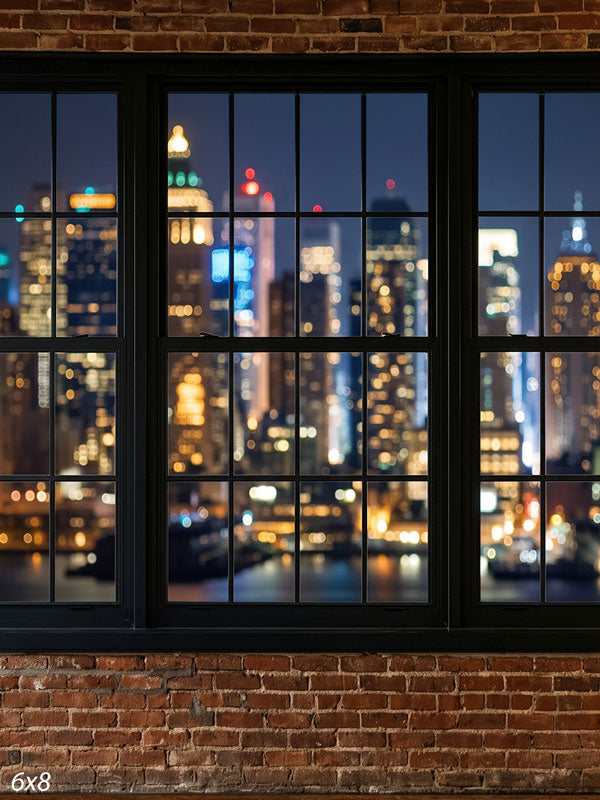 Industrial loft with an exposed red-brick wall and black-framed windows over a nighttime city skyline in soft bokeh, an urban photography backdrop.