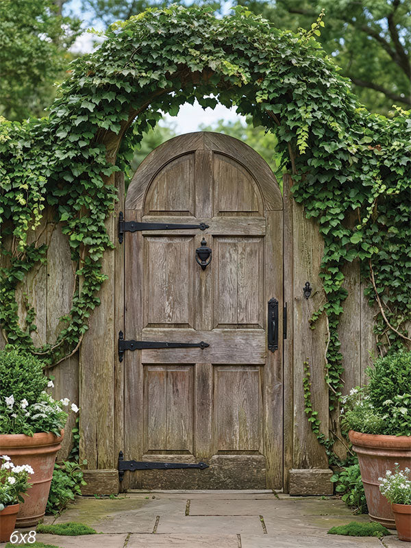 Photography backdrop featuring a weathered wooden garden gate framed by an ivy-covered arch, with fence panels and potted greenery creating a garden setting.