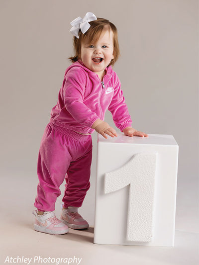 Toddler milestone session on light gray backdrop with large “1” block—popular for cake smash and family photographers.