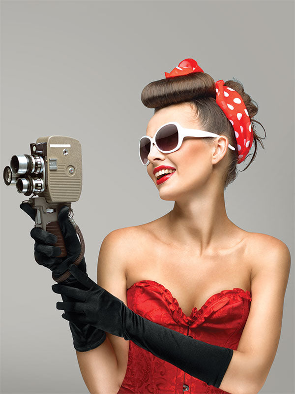 Retro-style model posing with camera in front of smooth light gray backdrop—ideal for creative or themed portrait work.