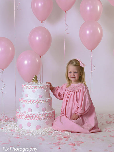 Smooth light gray seamless paper backdrop frames a pink birthday cake photo setup with a smiling girl.
