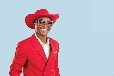 Male model wearing a red suit posing in front of a light blue seamless photography backdrop paper in a studio setting.
