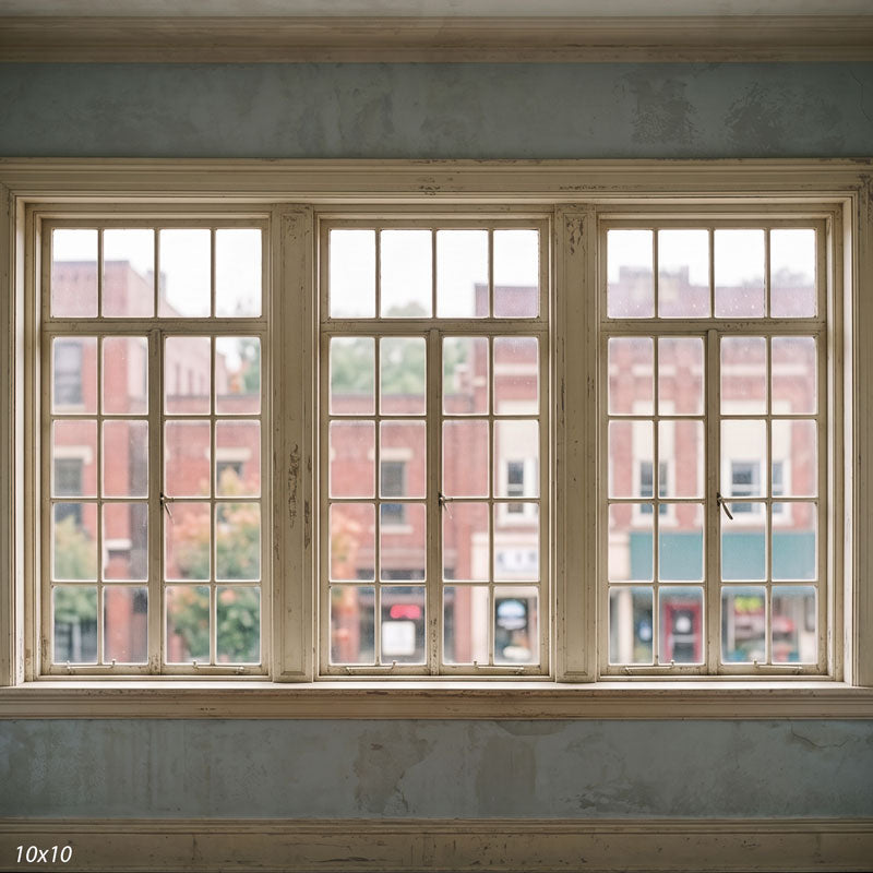 Wider view showing three distressed cream windows, a sage-green wall, and the blurred small-town storefronts beyond, a vintage photography backdrop.