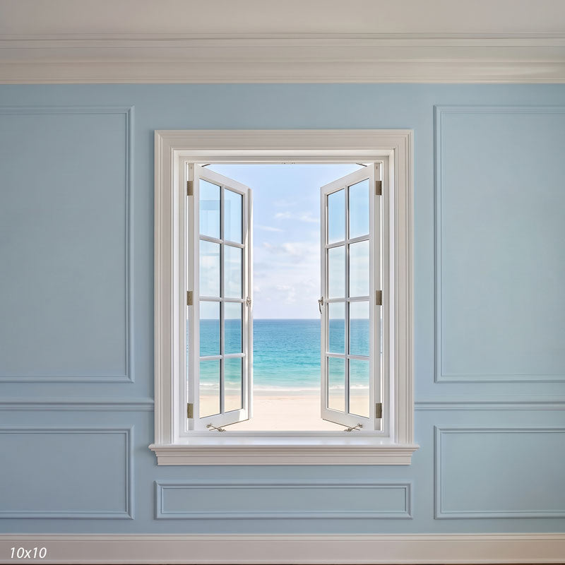 Wider view showing the open window smaller within more of the pale blue paneled wall with its molding, a coastal photography backdrop.