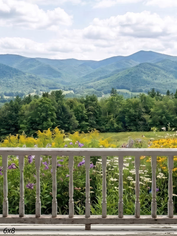Summer mountain photography backdrop with a white porch railing overlooking a wildflower meadow of purple and yellow blooms and rolling green mountains.
