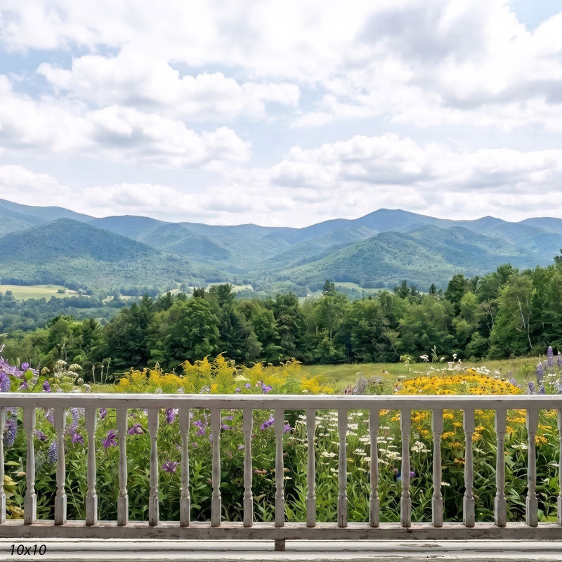 Summer mountain photography backdrop shown wider, with more sky, layered blue-green mountains, and a broad wildflower meadow behind the white railing.