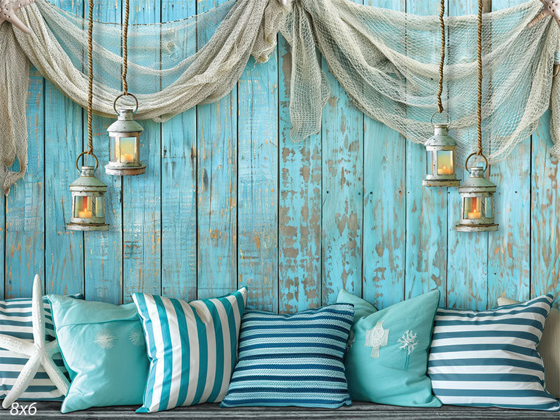 A nautical-themed backdrop featuring a distressed blue wooden wall, hanging lanterns, and striped pillows, ideal for cake smash and coastal-themed photography.