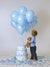 Boy looks up at floating blue balloons in front of a seamless gray backdrop during a styled birthday shoot.