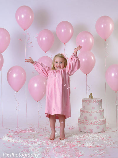 Subtle light gray paper backdrop behind festive pink balloons and girl in dress for birthday photo shoot.