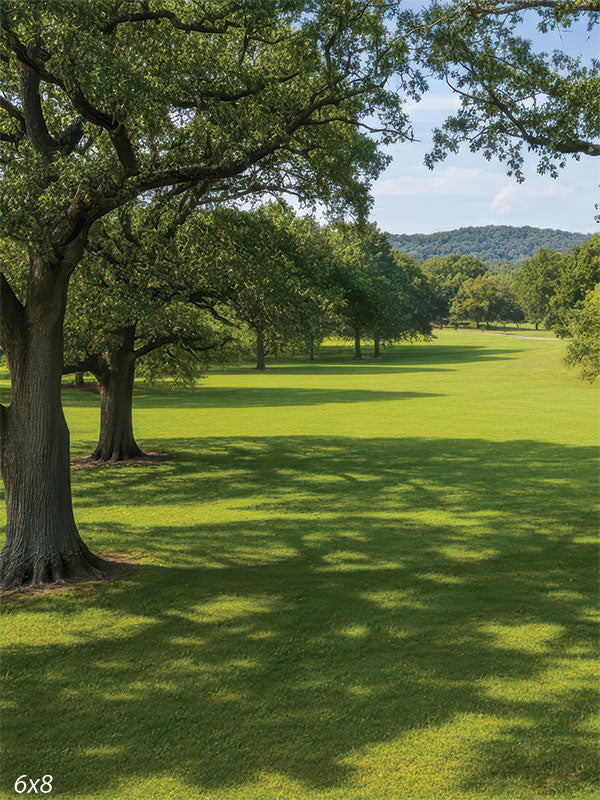 A scenic studio background showing two large oak trees framing a sunny green meadow. Shadows stretch across the manicured grass toward distant hills.