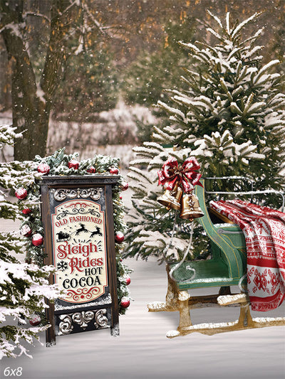 Old-Fashioned Sleigh Ride and Hot Cocoa Photography Backdrop - Vintage sleigh with festive decorations and a sign advertising sleigh rides and hot cocoa in a snowy winter scene.