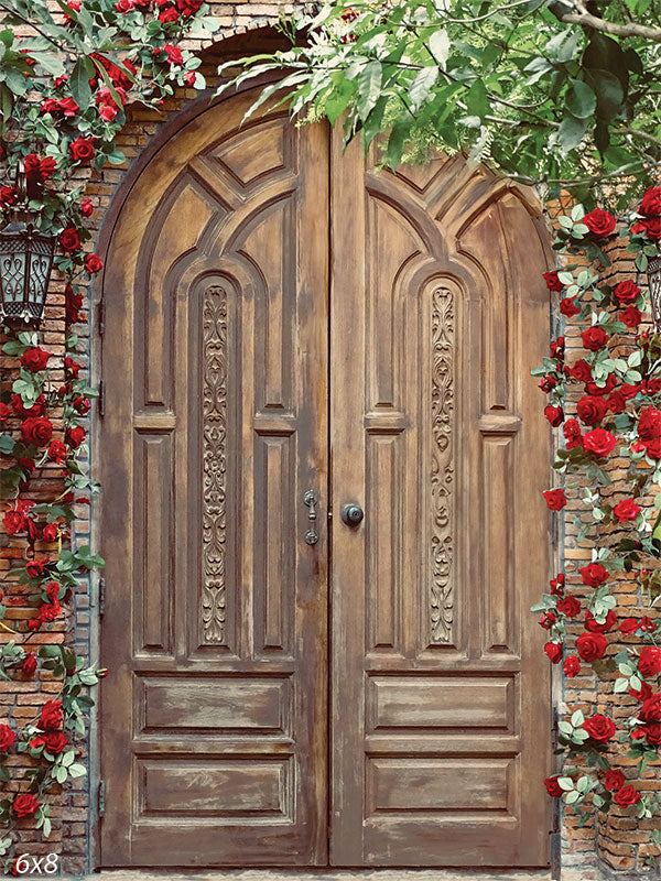 An ornate wooden door adorned with vibrant red roses and lush greenery, perfect for rustic and vintage-themed photography.