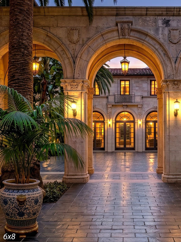Grand stone archways opening onto a lantern-lit Mediterranean villa courtyard at dusk with palms and a glazed urn, a scenic photography backdrop.