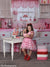 Young girl holds pink mixing bowl in a charming Valentine kitchen setup featuring red accents and heart-themed props.