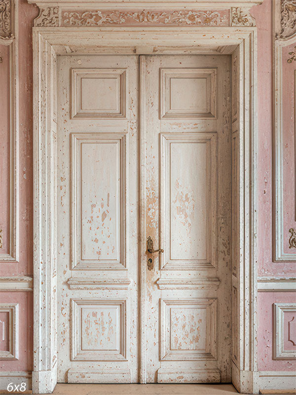 This photography backdrop features distressed ivory double doors centered in a blush pink paneled wall with ornate relief details and muted gold accents as a studio background.