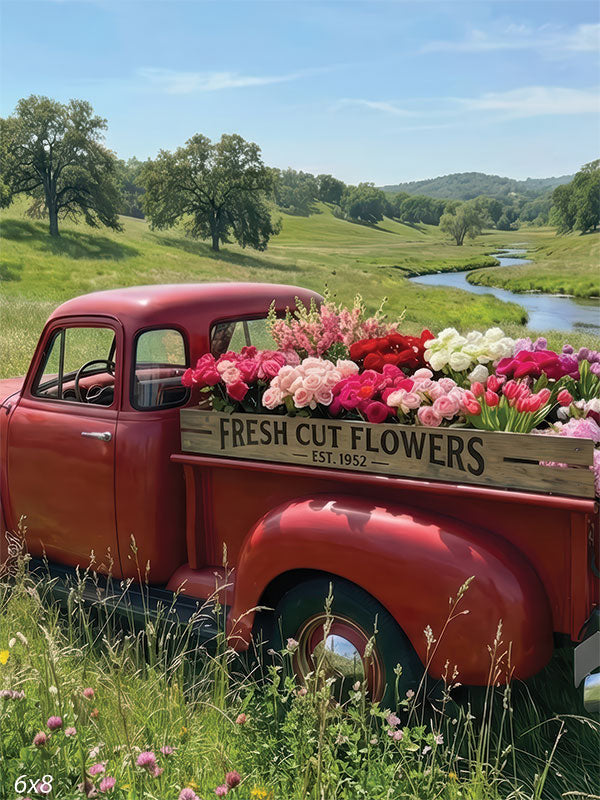 A studio background showing a red vintage truck filled with colorful flowers in a green meadow. A stream winds through hills under a blue sky.