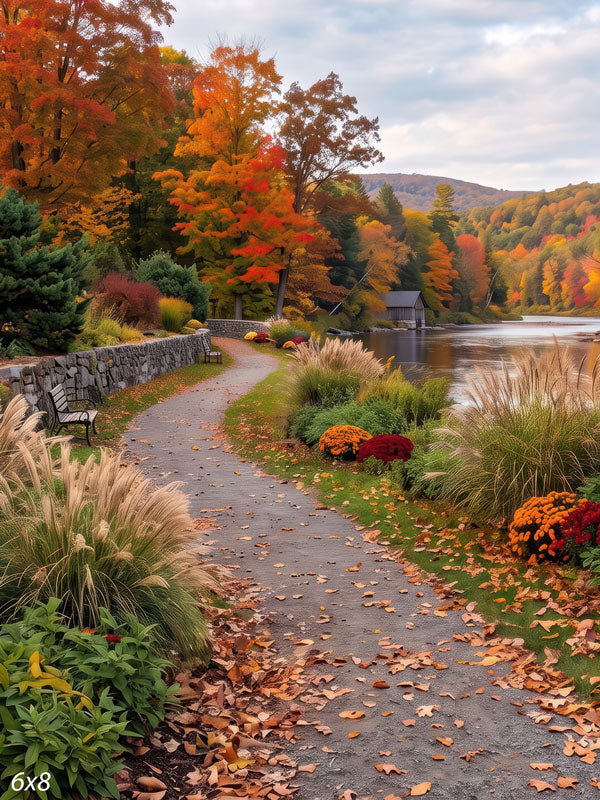 Autumn riverside photography backdrop with a curving gravel path along a stone wall, ornamental grasses, mums, and peak fall trees beside a calm river.